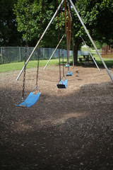 Empty Swing Set on Elementary School Playground Surrounded by Lush Spring Foliage