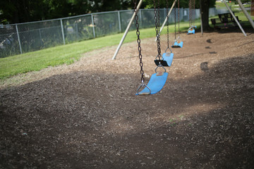 Empty Swing Set on Elementary School Playground Surrounded by Lush Spring Foliage