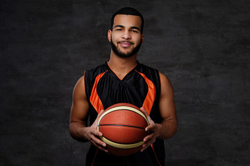 Smiling African-American basketball player in sportswear isolated over dark background.