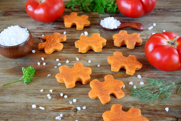 Puzzle shaped salty cookies with paprika and tomato paste surrounded by the ingredients