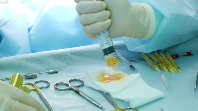 The doctor drains the syringe onto the cheesecloth, the human fat collected during the plastic surgery