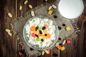 Obraz na płótnie Canvas Cottage cheese with candied fruit, raisins, peanuts and glass of milk or kefir on dark wooden background. Healthy food for breakfast, snack or dinner.