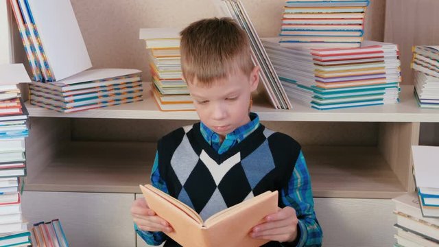 Seven-year-old boy attentively reads the book sitting among books.