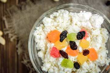 Cottage cheese with candied fruit, raisins, peanuts and glass of milk or kefir on dark wooden background. Healthy food for breakfast, snack or dinner.