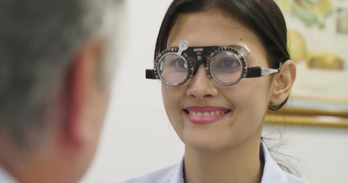 Asian senior male optometrist gives pair of optometry glasses to beautiful asian women.