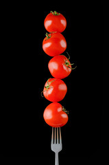 close up view of levitating cherry tomatoes on fork isolated on black
