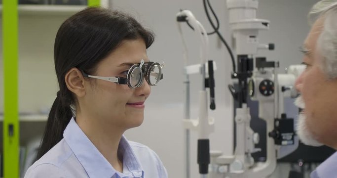 Asian senior male optometrist gives pair of optometry glasses to beautiful asian women.