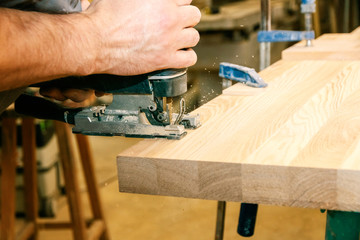 Man Sawn a Wooden Board with an Electric Jigsaw close-up.