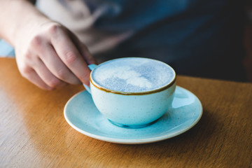 Man holding blue matcha tea latte in cafe.