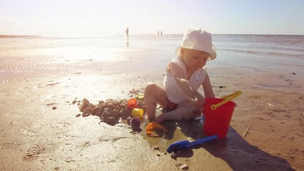 child on the beach playing with sand and toys