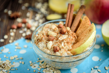 Homemade oatmeal with apple, cinnamon, hazelnuts, honey and peanuts on dark wooden background. Healthy breakfast.