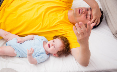 Young father with his 7 month old little son dressed in pajamas are relaxing and playing in the bed at the weekend together, lazy morning, warm and cozy scene.