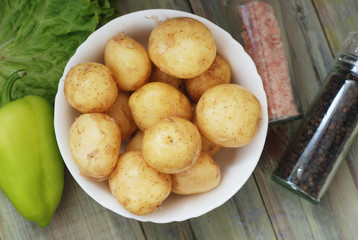 New Raw Potatoes in Bowl on Rustic Wooden table. Close up view, Wooden Spoons, over Wooden Background.