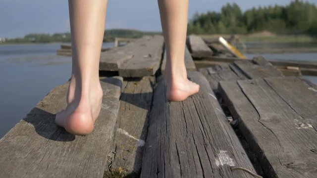 boy with his bare feet walking along the old decrepit pier