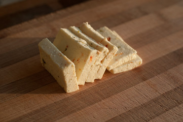 Sliced Cheese with pieces of paprika on wooden bamboo cutting board at home kitchen in morning
