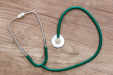 A green stethoscope is lying on a wooden table