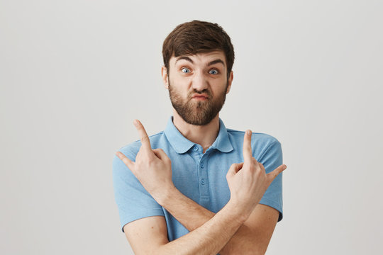 Excited Caucasian Guy Standing With Crossed Hands And Rock Gestures With Tensed Face As If Trying To Act Cool, Staring At Camera Over Gray Background. Cute Man Tries To Convince People He Can Be Scary