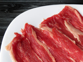 Raw beef steaks on white plate. Bacon slices close-up