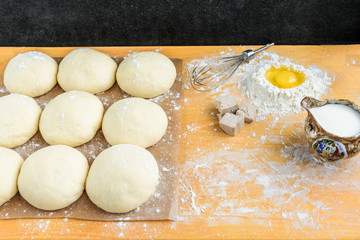 Baking background top view. Making sweet bun or bread dough. Cooking ingredients for pastry on wooden board with dough, egg, yeast, milk, flour. Culinary classes or recipe concept.