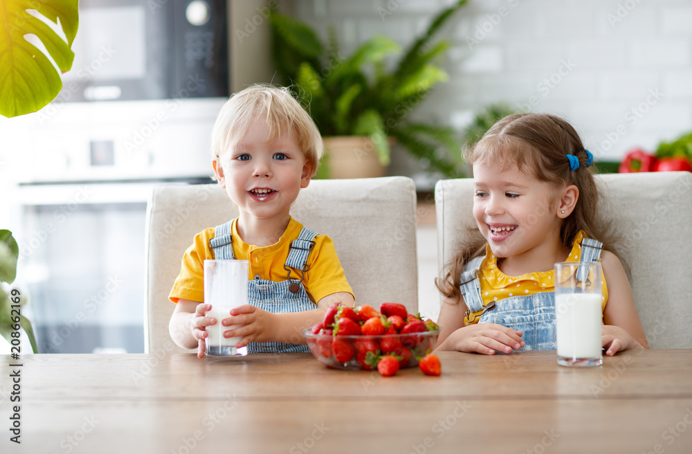 Wall mural happy children brother and sister eating strawberries with milk