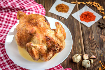 Roasted chicken on dark wooden background with spices and garlic.