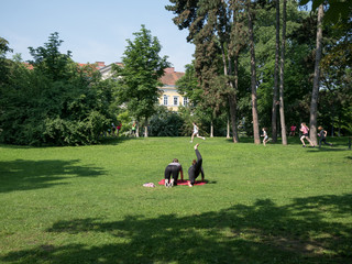 In the park: two young women doing workout on a mat and young girls running in the background