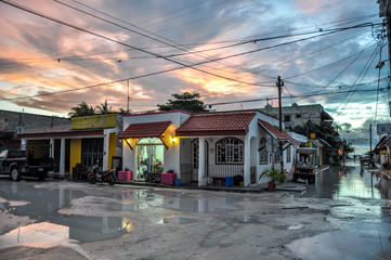 Fototapeta na wymiar HOLBOX, MEXICO - MAY 25, 2018: Flooded sand roads in the main square of Isla Holbox with tourists and Caribbean houses and shops during sunset