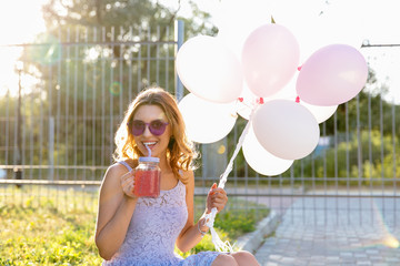 Charming pretty girl with air balloons drinking a fresh beverage, enjoying the sunny days, while walking outdoors.