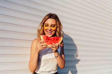 Pretty girl eating a watermelon, wearing yellow sunglasses, enjoying the summer days, outdoors. - obrazy, fototapety, plakaty