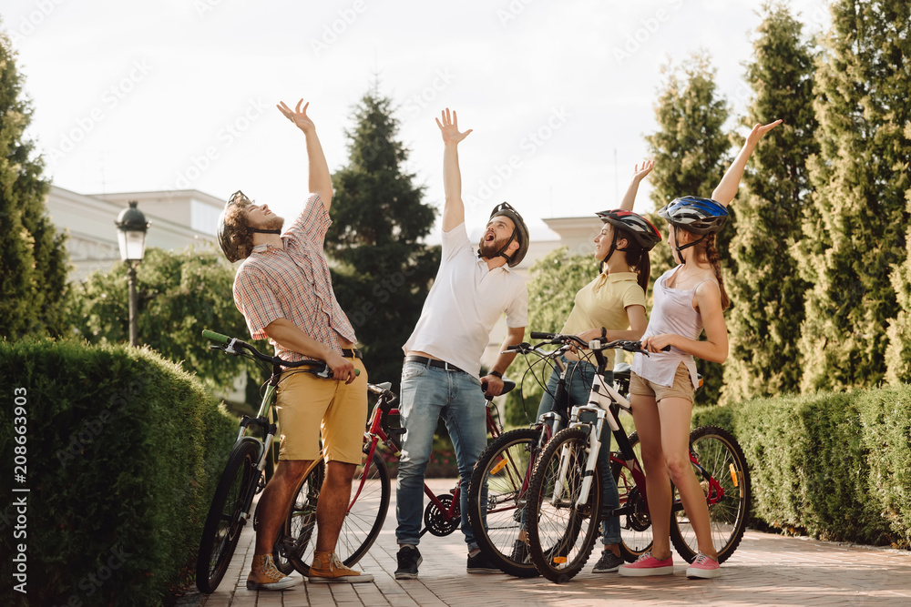 Wall mural group of happy people resting outdoors. four friends with bicycles having fun in summer park. summer