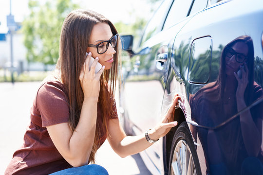 Yougn woman inspecting her scratched car and calling insurance agent