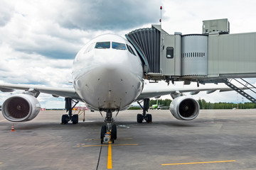 Commercial passenger airplane in the parking at the airport with a nose forward and a gangway - front view.