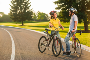 Couple of students with bikes outdoors. Happy couple with bikes is smiling and looking at each other on the road. Perfect summer date.