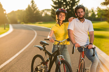Obraz premium Happy couple looking at camera outdoors. Young students in love resting with bicycles on the road. People, leisure and lifestyle.