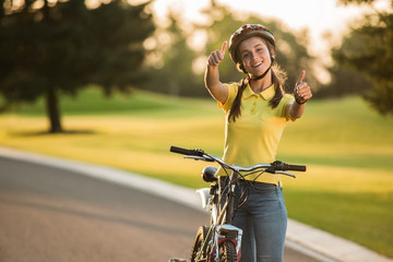 Attractive woman cyclist giving two thumbs up. Happy joyful female student with bicycle gesturing thumb up with two hands outdoors. People, positive emotions and lifestyle.
