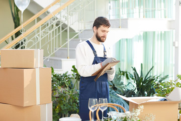 Serious concentrated handsome young moving company specialist keeping records while examining goods at place of delivery