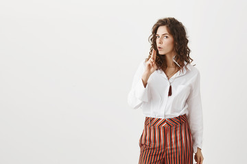 Girl working as secret agent, making shot and blowing gun after completing mission. Serious good-looking caucasian woman with curly hair, showing finger gun gesture near face, gazing assured at camera