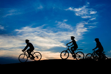 Fototapeta na wymiar Friends riding bicycles at sunset sky. Silhouettes of three students cycling on hill on evening sky background. People and active leisure.