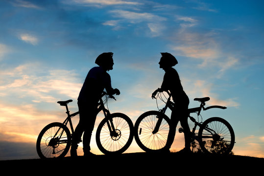 Silhouette of couple on romantic date. Young couple with bikes standing on hill at evening sky. Enjoying of each other.