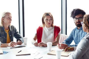 Serious concentrated multiethnic business colleagues attentively listening to team member while...