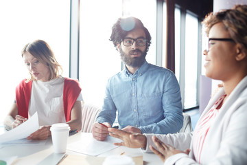 Confident handsome bearded male manager in glasses asking colleague about project while thinking of...