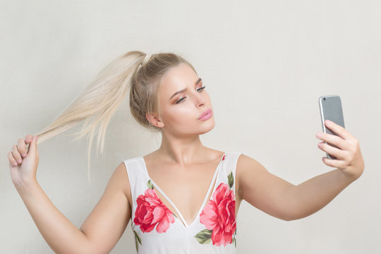 Fashionable blonde model with natural makeup and blonde hair taking self portrait on her mobile phone