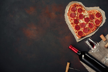 Heart shaped pizza with mozzarella, sausagered with a bottle of wine and wineglas. Valentines day greeting card on rusty background