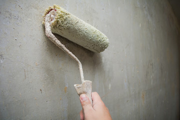 Close-up hand holds rolling paint brush, painting interior stucco wall with white color.Preparation...
