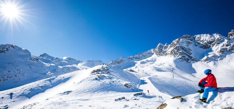 Young happy skier sitting on the top of mountains and enjoying view of Rhaetian Alps, Tonale pass, Italy, Europe
