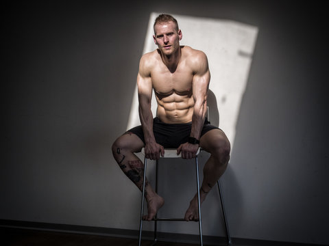 Attractive shirtless blond male bodybuilder in shorts indoors in