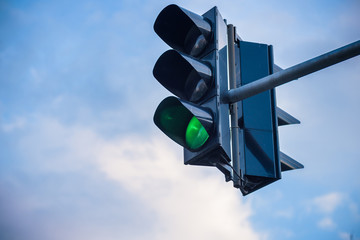 The green streetlight signal with cloudy blue skies in the background