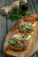 Antipasto bruschetta set made of toasted bread with tomato, meat pate, olives, cream cheese and tuna salad. Classic Italian appetizers on a rustic table.