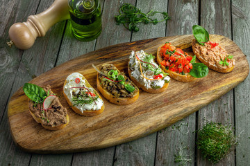 Classic Italian antipasti bruschetta set made of baguette tomato, meat pate, olives, cream cheese and tuna salad on a rustic wooden board. Top view.