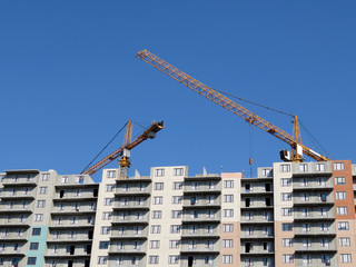Construction cranes over the panel building under construction, unfinished house. Construction site, clear blue sky
